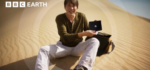 Professor Cox, showcasing a circular object, with a bag beside him in a desert environment.